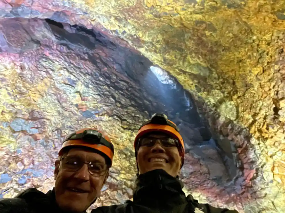 Two visitors under an overhang of gold rock with a lamp behind