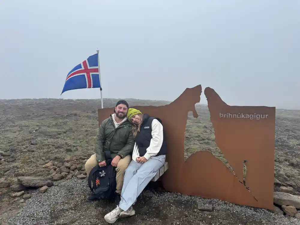 Two visitors at the Thrihnukagigur marker with an Icelandic flag in fog